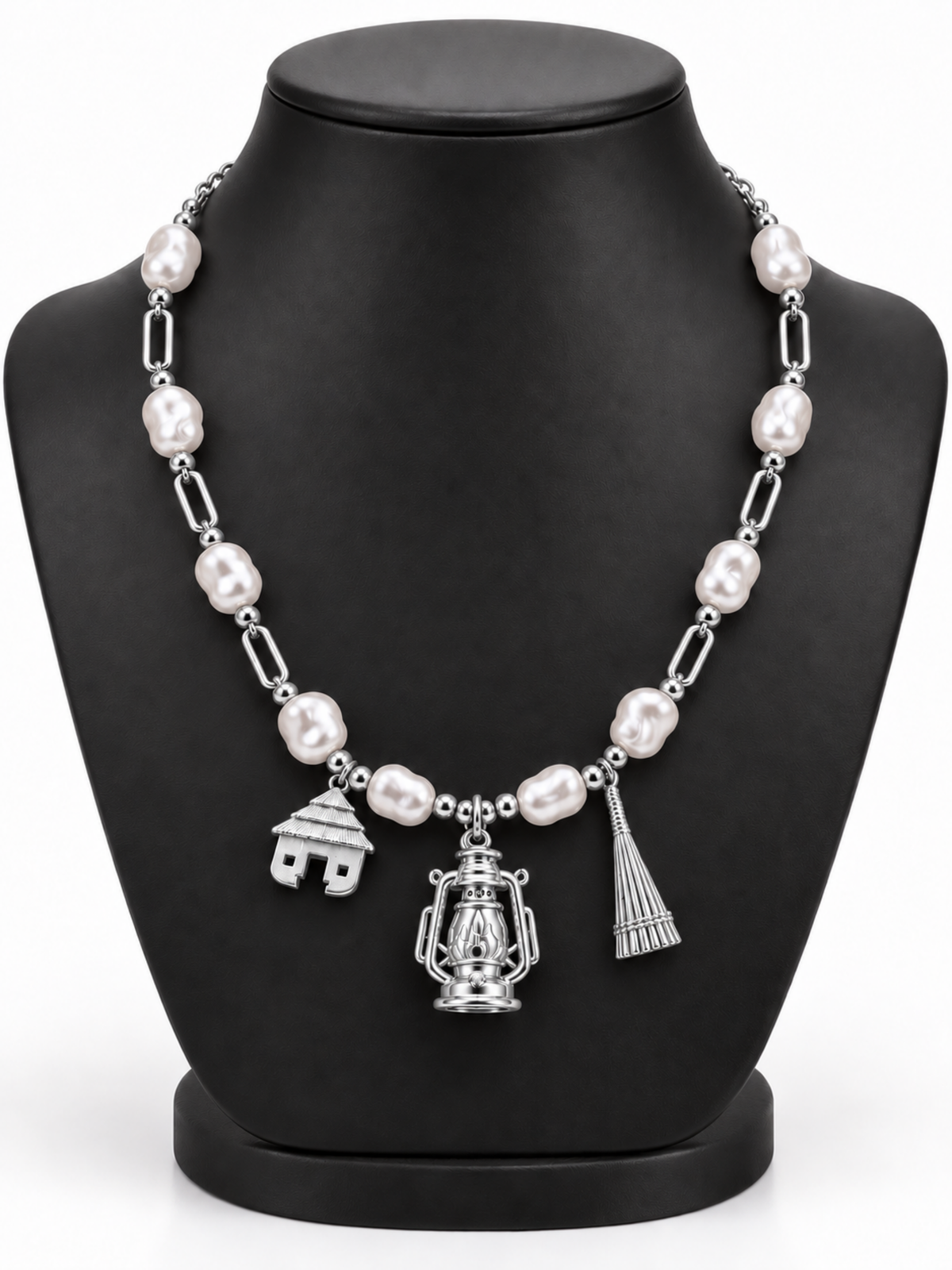 Villager Roots silver-colour necklace with ten pearl-effect acrylic beads and hut, lantern and broom pendants, on a black display bust
